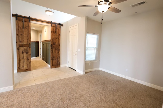 empty room featuring a barn door, light colored carpet, and ceiling fan