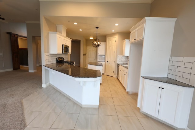 kitchen with white cabinets, hanging light fixtures, kitchen peninsula, stainless steel appliances, and a barn door