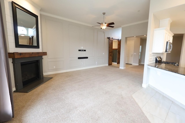 unfurnished living room featuring crown molding, a barn door, light carpet, ceiling fan, and a fireplace