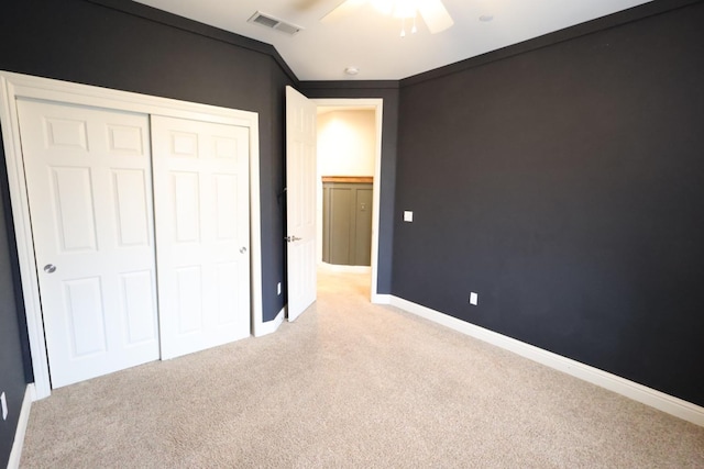 unfurnished bedroom featuring ceiling fan, light colored carpet, ornamental molding, and a closet