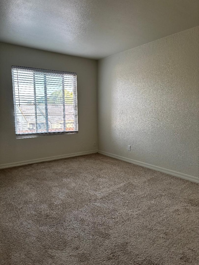 carpeted spare room with a textured ceiling, baseboards, and a textured wall