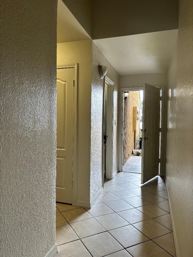 hall with baseboards, a textured ceiling, light tile patterned flooring, and a textured wall