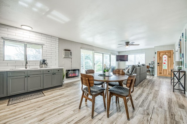 dining area featuring sink, a wall unit AC, ceiling fan, and light hardwood / wood-style flooring