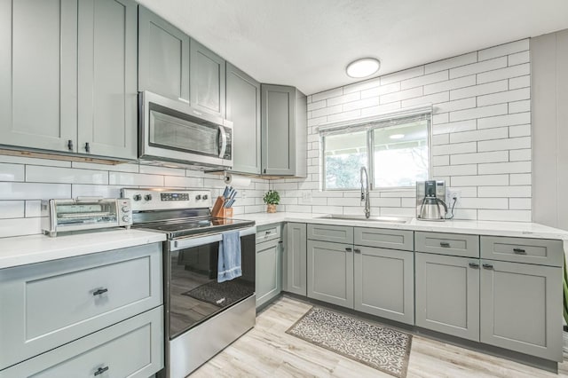 kitchen with sink, light hardwood / wood-style flooring, gray cabinets, appliances with stainless steel finishes, and backsplash