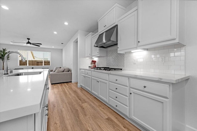 kitchen with sink, backsplash, ventilation hood, white cabinets, and light wood-type flooring