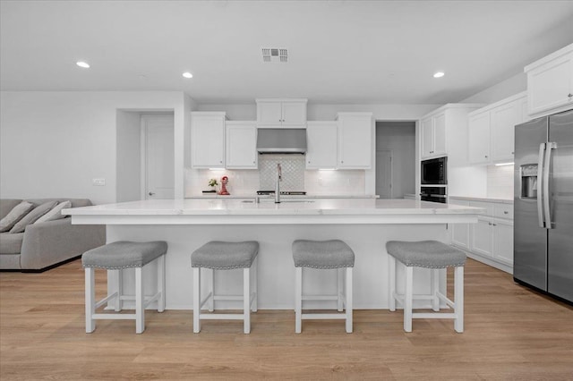 kitchen with white cabinetry, a breakfast bar, a kitchen island with sink, and black appliances