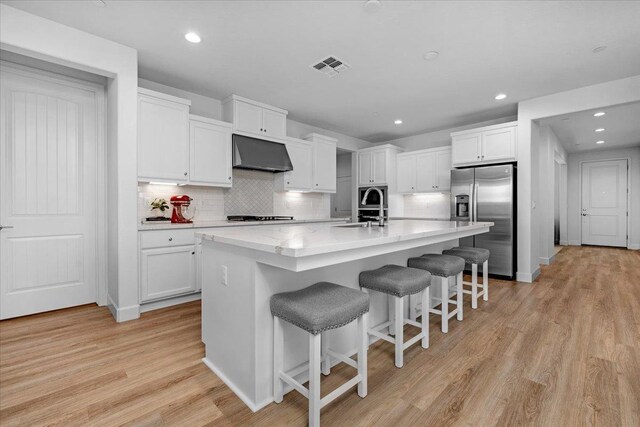 kitchen featuring a kitchen bar, white cabinetry, stainless steel fridge with ice dispenser, range hood, and a kitchen island with sink