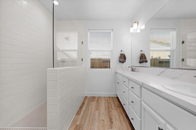 bathroom with wood-type flooring, a tile shower, and vanity