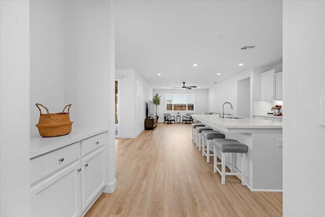 kitchen with tasteful backsplash, sink, white cabinets, a kitchen breakfast bar, and light hardwood / wood-style flooring