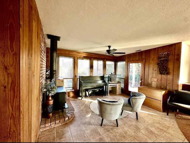 interior space featuring a healthy amount of sunlight, a wood stove, ceiling fan, and wood walls