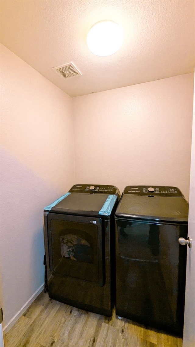 laundry area featuring light hardwood / wood-style flooring, washing machine and dryer, and a textured ceiling