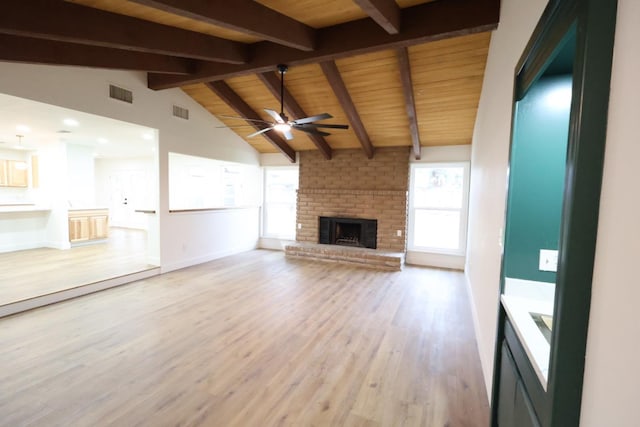 unfurnished living room featuring a brick fireplace, a healthy amount of sunlight, vaulted ceiling with beams, and light hardwood / wood-style floors