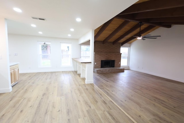 unfurnished living room with a fireplace, lofted ceiling with beams, ceiling fan, and light wood-type flooring