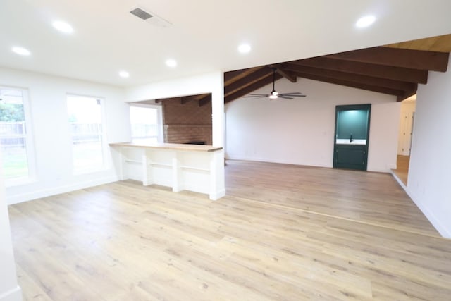 unfurnished living room featuring sink, lofted ceiling with beams, a brick fireplace, light hardwood / wood-style flooring, and ceiling fan