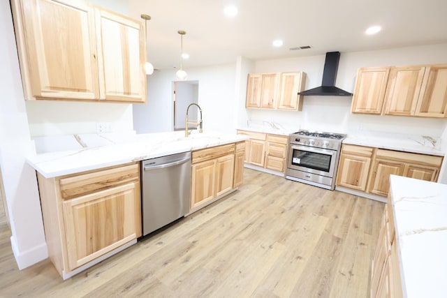 kitchen featuring light brown cabinetry, sink, hanging light fixtures, stainless steel appliances, and wall chimney range hood