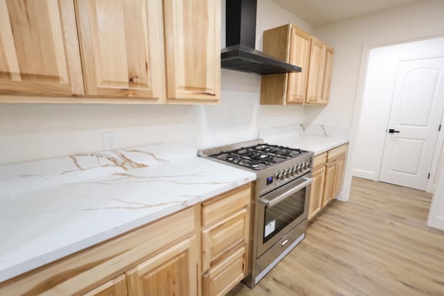 kitchen with wall chimney exhaust hood, high end stainless steel range, light hardwood / wood-style flooring, light brown cabinets, and light stone countertops