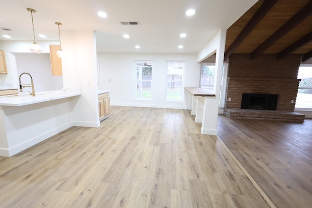 unfurnished living room with a brick fireplace, sink, a wealth of natural light, and light wood-type flooring