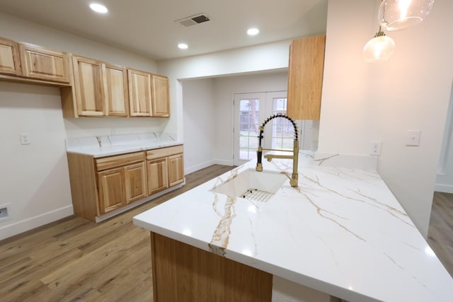 kitchen featuring sink, light stone counters, decorative light fixtures, kitchen peninsula, and light wood-type flooring