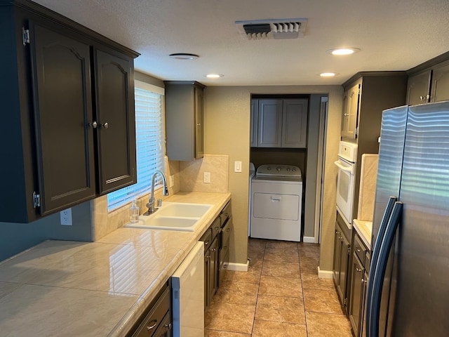 kitchen with tile countertops, visible vents, a sink, washer / dryer, and white appliances