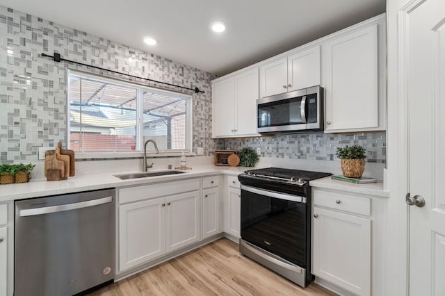 kitchen with sink, appliances with stainless steel finishes, backsplash, light hardwood / wood-style floors, and white cabinets