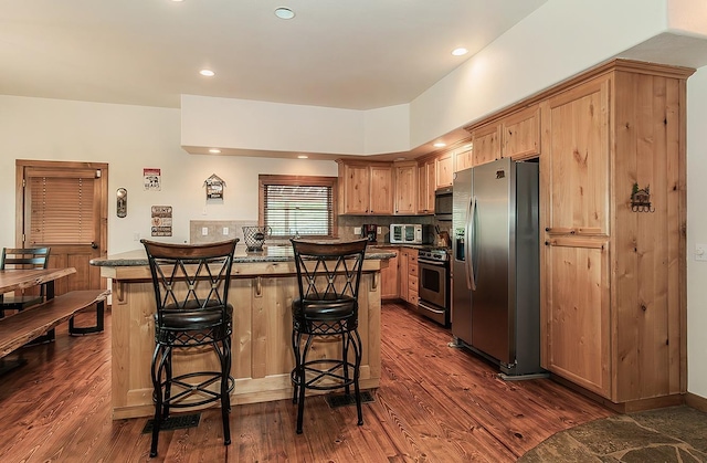 kitchen with stainless steel appliances, a kitchen island, a breakfast bar, and dark hardwood / wood-style flooring
