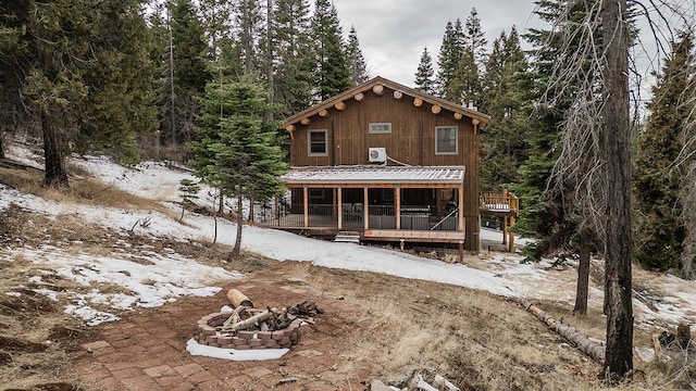 snow covered back of property with covered porch and a fire pit