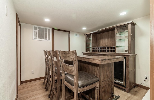 bar with dark brown cabinetry, light hardwood / wood-style flooring, and a textured ceiling