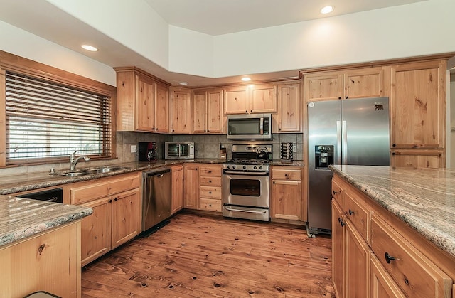 kitchen featuring sink, decorative backsplash, stainless steel appliances, light stone countertops, and light wood-type flooring