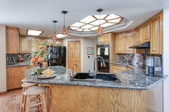 kitchen featuring sink, decorative light fixtures, kitchen peninsula, a raised ceiling, and black appliances