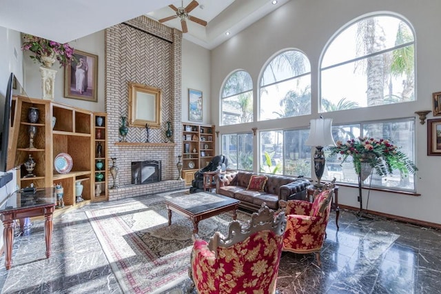 living room with ceiling fan, plenty of natural light, a fireplace, and a high ceiling