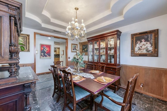 dining area featuring a tray ceiling, a chandelier, and wood walls