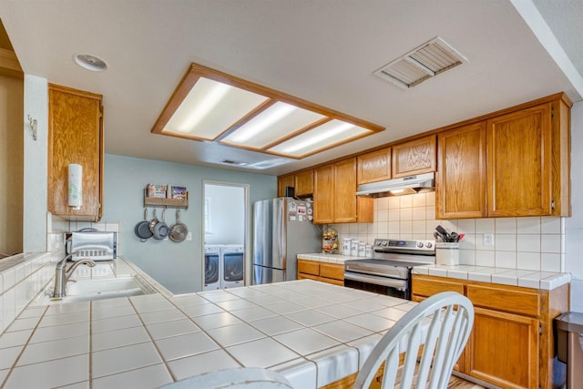 kitchen with appliances with stainless steel finishes, washer and dryer, tasteful backsplash, sink, and tile counters