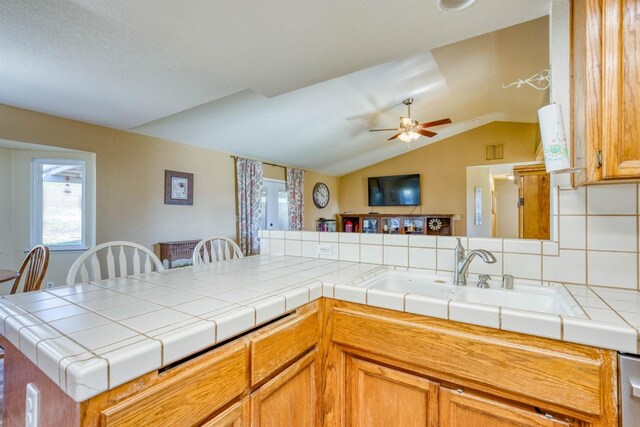 kitchen featuring lofted ceiling, sink, tile counters, and kitchen peninsula