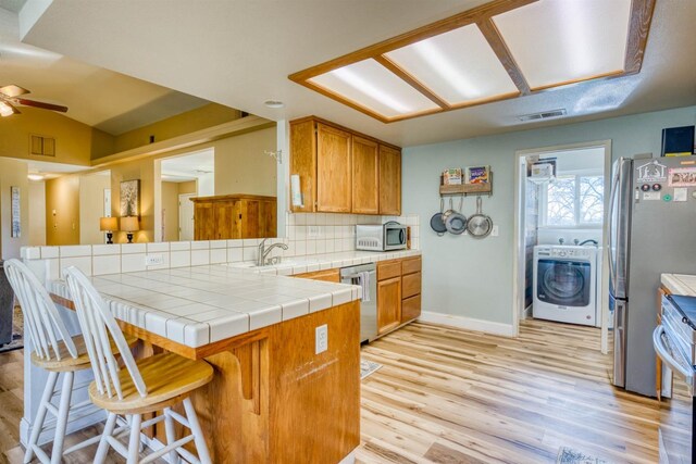 kitchen featuring appliances with stainless steel finishes, a breakfast bar, tile countertops, washer / dryer, and kitchen peninsula