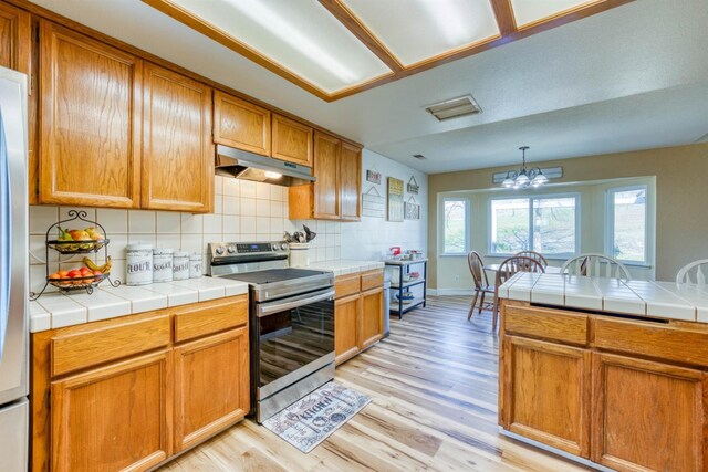 kitchen with light hardwood / wood-style flooring, hanging light fixtures, tasteful backsplash, tile counters, and stainless steel electric range oven