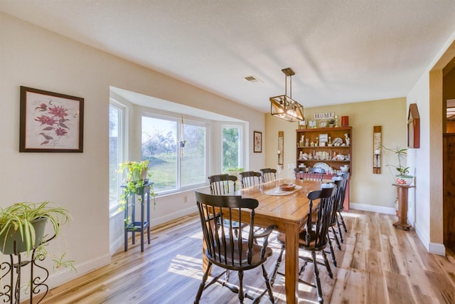 dining room with a notable chandelier, a textured ceiling, and light wood-type flooring