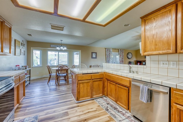 kitchen featuring appliances with stainless steel finishes, tile countertops, hanging light fixtures, kitchen peninsula, and light wood-type flooring