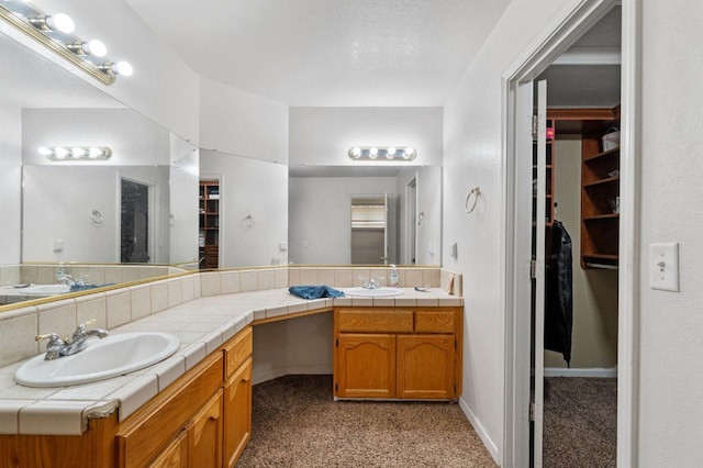bathroom featuring a walk in closet, double vanity, and a sink