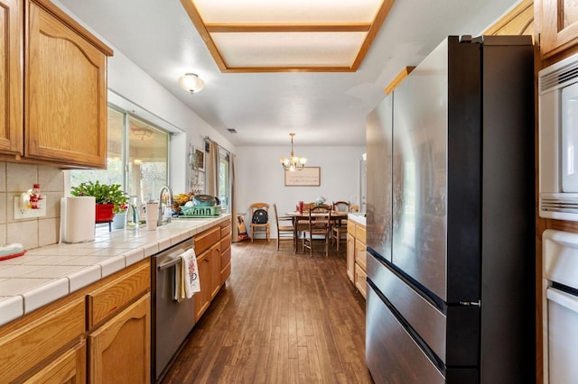 kitchen featuring tasteful backsplash, an inviting chandelier, stainless steel appliances, a sink, and dark wood-type flooring