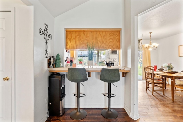 kitchen with a kitchen breakfast bar, an inviting chandelier, vaulted ceiling, tile countertops, and wood finished floors