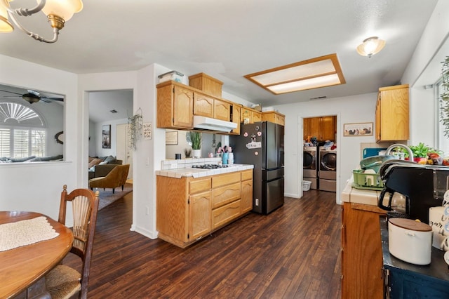 kitchen featuring dark wood-style floors, tile counters, under cabinet range hood, washing machine and dryer, and freestanding refrigerator