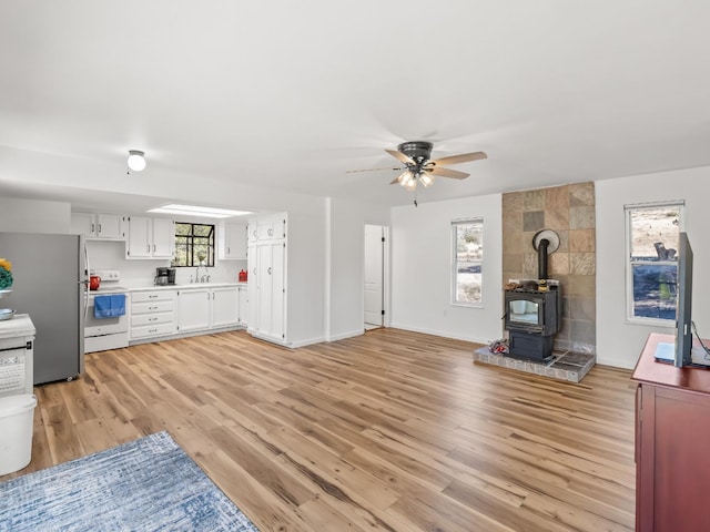 living room with sink, light hardwood / wood-style floors, ceiling fan, and a wood stove