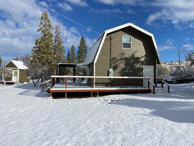 snow covered back of property with a wooden deck and a storage shed