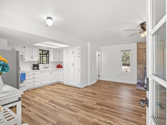 kitchen featuring white electric range oven, sink, white cabinetry, light hardwood / wood-style flooring, and stainless steel refrigerator