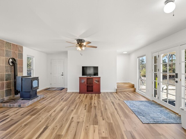 unfurnished living room with ceiling fan, a wood stove, and light wood-type flooring