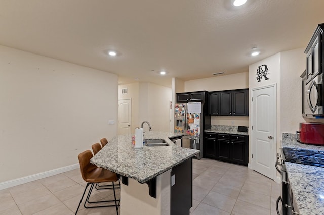 kitchen with light stone counters, a kitchen bar, an island with sink, and appliances with stainless steel finishes