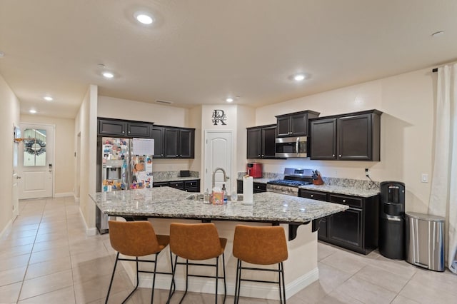 kitchen featuring an island with sink, appliances with stainless steel finishes, light stone counters, and a kitchen breakfast bar