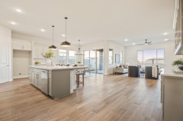 kitchen with hanging light fixtures, stainless steel dishwasher, light hardwood / wood-style floors, and a center island with sink