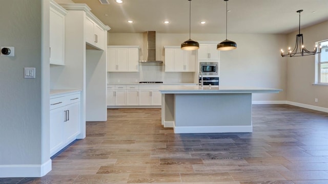 kitchen featuring white cabinetry, wall chimney range hood, pendant lighting, and appliances with stainless steel finishes