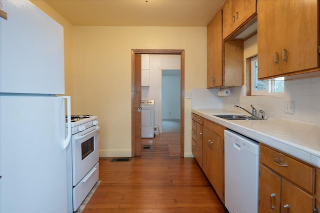 kitchen with sink, white appliances, light hardwood / wood-style flooring, backsplash, and washer / clothes dryer